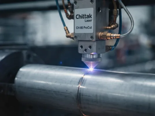 Macro close-up of a Chittak laser cutting head precision-cutting an 80mm stainless steel round tube, with brilliant blue laser contact and tiny sparks.